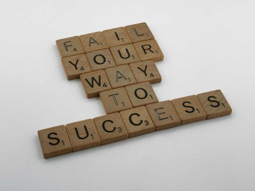 Wooden tiles spell 'Fail Your Way to Success' emphasizing perseverance.