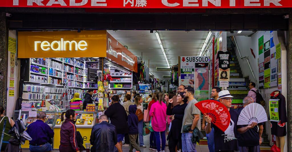 Crowded trade center with diverse shoppers and colorful market stalls bustling with activity.
