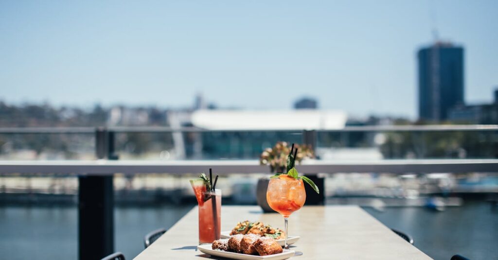 Delicious meat loaf served near colorful alcoholic cocktails on table on sunny terrace of cafeteria near river on blurred background